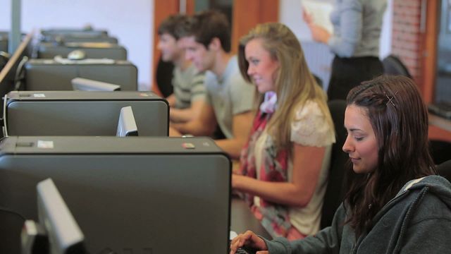 Students diligently using computers in a university classroom highlighting technology in education. Suitable for illustrating educational technology, collaborative learning, or classroom environment in promotional material and articles on higher education.