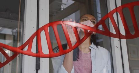 Masked researcher touching glass through red dna helix overlay, pandemic genetics concept