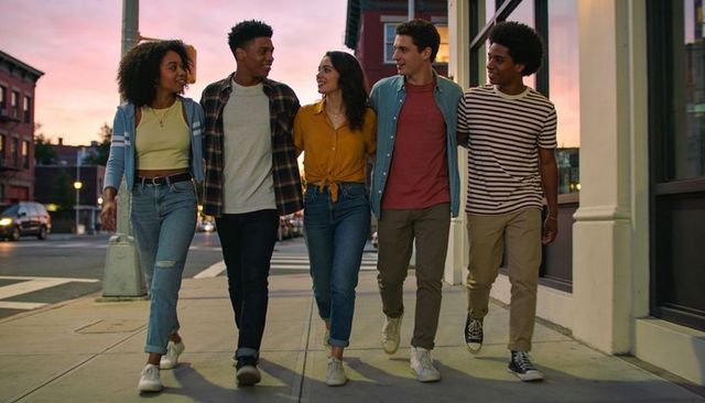 Diverse young friends walking and laughing on urban sidewalk at sunset