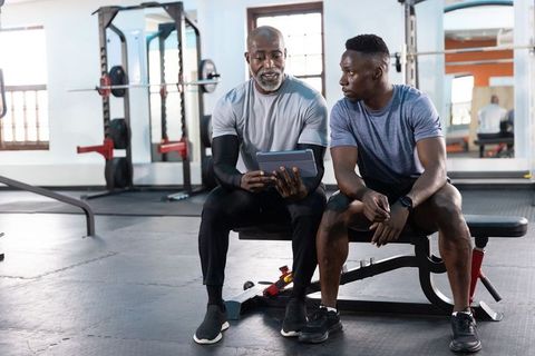 African american personal trainer coaching client with tablet on gym bench