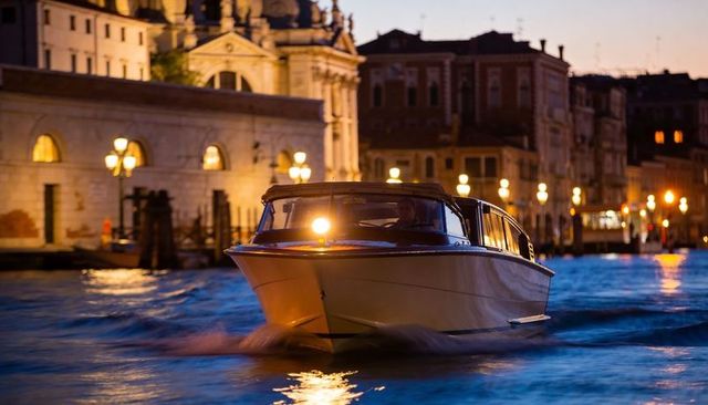 Motorboat gliding through venice canal at dusk with warm waterfront lights and historic facades