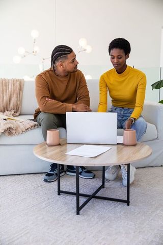 Diverse couple collaborating in modern living room on laptop
