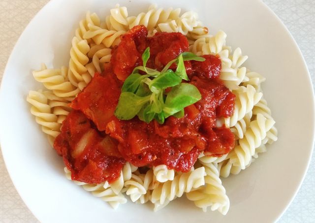 Fusilli pasta topped with rich tomato sauce and fresh basil garnish. Perfect for food blogs, restaurant menus, recipe illustrations, and culinary articles.