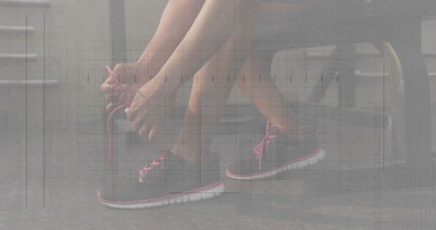 Athlete tying pink shoelaces on dark running shoes while sitting on gym bench