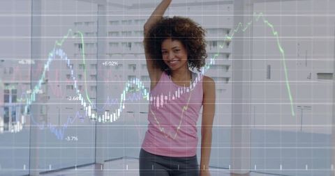 Smiling woman raising arm with financial chart overlay in bright modern studio