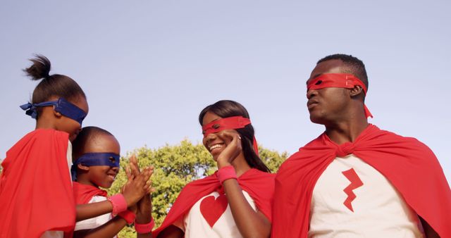 African American family dressed as superheroes, with copy space, stands confidently under a clear sky. Their matching red capes and masks symbolize unity and strength, evoking a playful and empowering atmosphere.