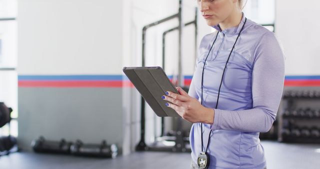 Image of concentrating caucasian female fitness trainer using tablet at a gym. Exercise, fitness and healthy lifestyle.