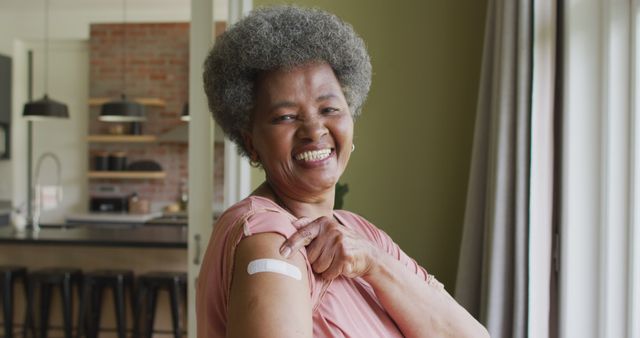 Happy african american senior woman showing plaster on arm after covid vaccination. senior health and lifestyle during covid 19 pandemic.