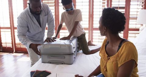 African american family packing silver suitcase on bed preparing for sunny vacation trip
