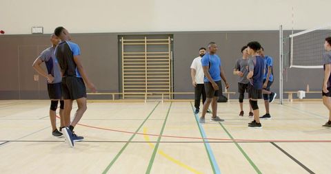 Diverse male volleyball team practicing indoor court drills with coach, teamwork training
