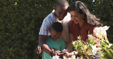 Parents and child tending sunlit backyard flowers, family bonding while gardening together