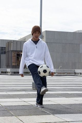 Asian teen male controlling soccer ball on urban rooftop plaza, dribbling in beanie hoodie