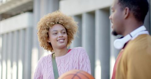Young friends smiling and chatting on campus holding basketball near modern concrete columns