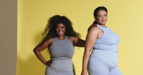 Inclusive curvy confidence duo wearing fitted activewear on vibrant yellow backdrop