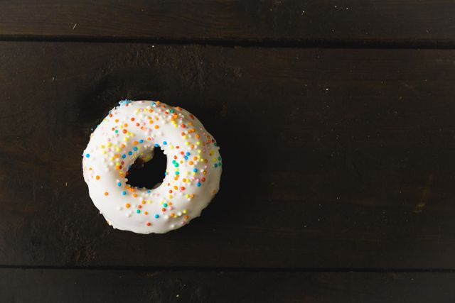 Directly above view of fresh white donut with sprinkler over black wooden table - Download Free Stock Photos Pikwizard.com