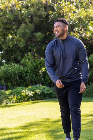 African american man walking and smiling in sunlit garden wearing dark athleisure