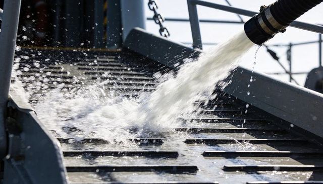 High-pressure water jet spraying onto metal grated ramp on ship deck during washdown