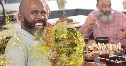 Smiling bearded man enjoying lively home dinner with friends and golden glitter effect