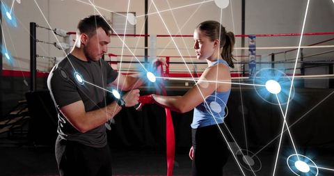 Coach wrapping boxer hands with red tape in boxing ring with futuristic network overlay