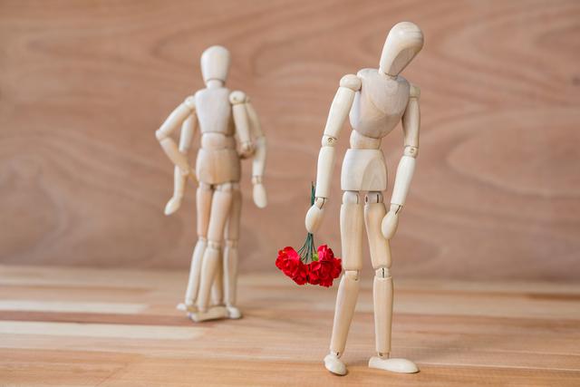 Conceptual depiction of depression and heartbreak with wooden mannequins. One mannequin holding flowers is walking away from a couple, looking dejected. Useful for illustrating themes of loneliness, rejection, mental health, and emotional struggles.