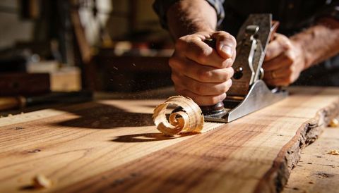 Woodworker planing live-edge board producing curled wood shavings in rustic workshop