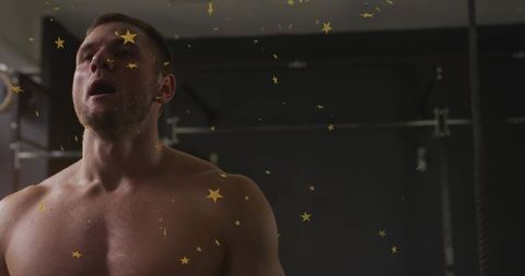 Shirtless athlete catching breath leaning back after intense weight training in dim gym