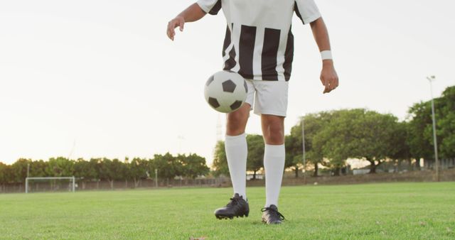Soccer player practicing ball control on a grassy field during sunset. Useful for promoting sports events, training camps, fitness programs, and illustrating active lifestyles.