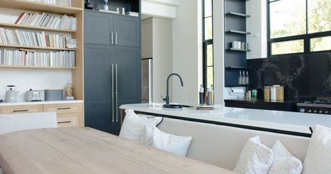 Contemporary open-plan kitchen with island banquette, oak table, matte faucet, tall windows
