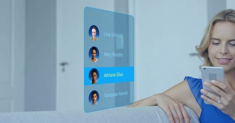 Woman holding smartphone selecting contact from holographic interface on living room couch