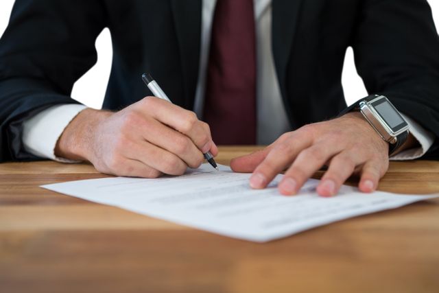 Businessman signing last will and testament form at desk. Ideal for use in articles about legal processes, estate planning, business agreements, and professional documentation. Suitable for illustrating concepts of legal work, contract signing, and professional business environments.