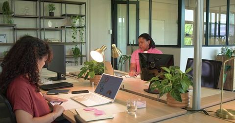 African american coworkers collaborating in modern biophilic open-plan office with laptops