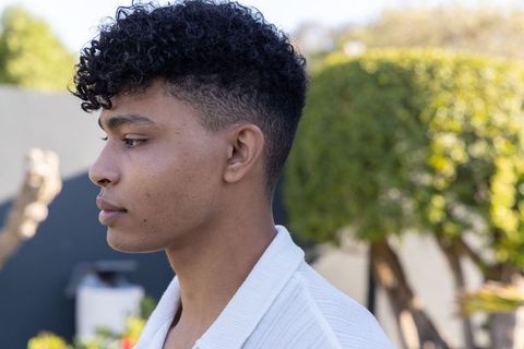 Side profile african american man wearing white textured cardigan sunlit courtyard