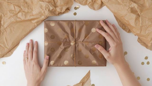 Wrapping gift with kraft paper and gold polka dots, hands adjusting twine overhead