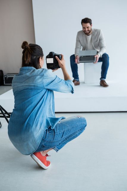 Male model posing with a laptop in a professional studio setting. Photographer capturing the moment with a camera. Ideal for use in articles about fashion photography, studio setups, professional modeling, or technology in creative industries.