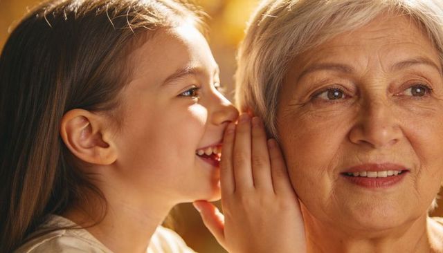 Granddaughter whispering to grandmother sharing secret moment closeup warm family bond