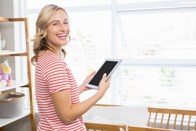 Smiling woman holding digital tablet in a bright, modern home. Ideal for use in lifestyle blogs, technology advertisements, home decor websites, and articles about modern living and technology integration in daily life.