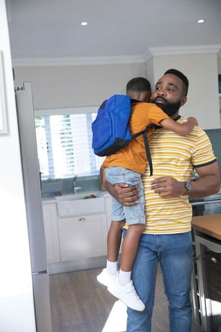 Father Hugging Son with Backpack in Kitchen at Home