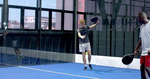 Diverse Men Engaged in Competitive Padel Match on Glass-Walled Court