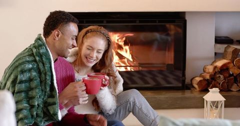 Cozy couple relaxing by fireplace with mugs