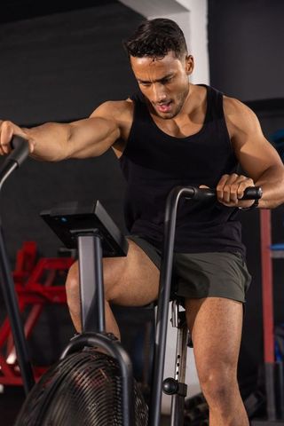 Male pushing through intense air bike workout building strength and endurance in gym