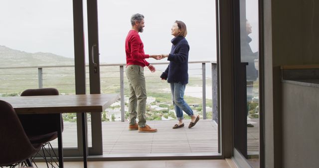 Couple enjoying a moment together, dancing on their balcony with a scenic mountain view in the background. Perfect for depicting romance, outdoor lifestyle, and joy of life in residential or vacation home advertising, travel brochures, and relationship counseling materials.