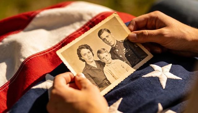 Holding vintage military family portrait on folded american flag, heritage and remembrance