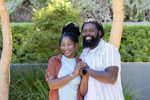 African american couple smiling and holding hands in sunlit courtyard showing watches