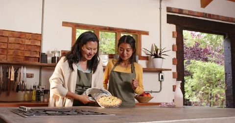 Mother and daughter baking pie together in rustic kitchen