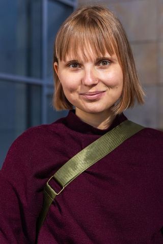 Young woman wearing burgundy sweater and olive crossbody strap smiling in urban portrait