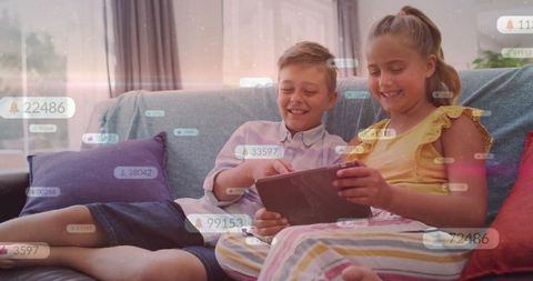 Preteen siblings smiling and sharing tablet with social notification bubbles on home couch