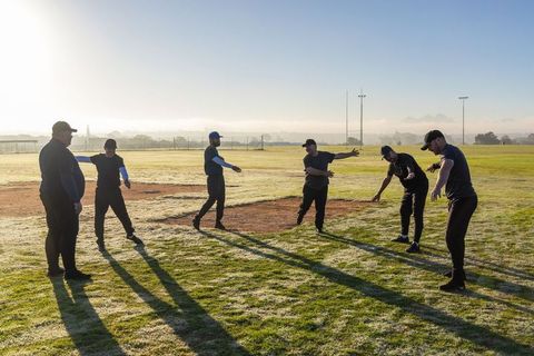 Morning baseball team warming up on dew-covered field at sunrise casting long shadows