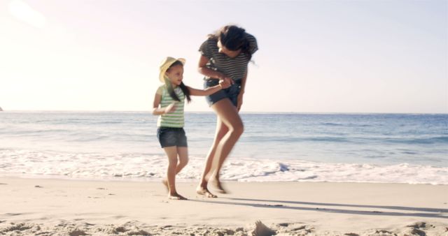 This image shows a mother and her daughter enjoying a moment together while walking along a sunny beach. It can be used for advertising family vacations, summer activities, or highlighting the bond between mothers and daughters. It is also suitable for social media posts, travel-related blogs, and lifestyle articles focusing on family time and outdoor enjoyment.