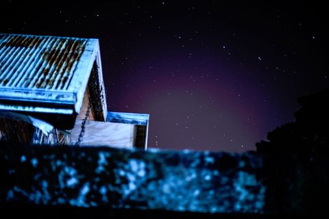 Rusting corrugated roof and mossy wall beneath violet starry night sky, moody rooftop scene