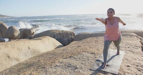 Woman Practicing Yoga Warrior Pose on Rocks by Ocean